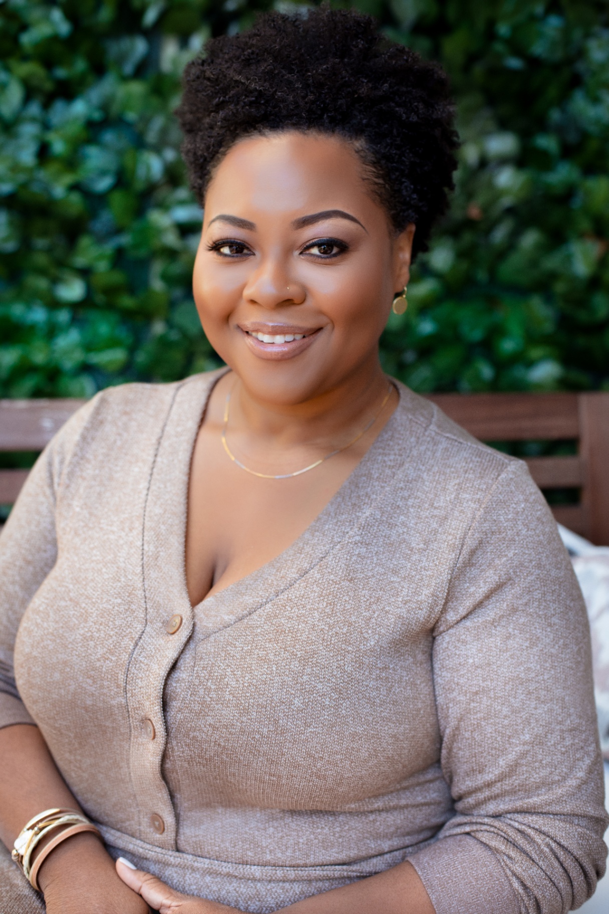 Zakiya Akerele standing outdoors in front of a green leafy hedge